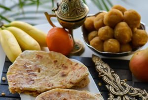 Traditional housewarming catering spread in Bangalore featuring Holige/Hobbattu, ripe bananas, sweet gulab jamun and ornate serving bowl, highlighting housewarming catering services near me Bangalore